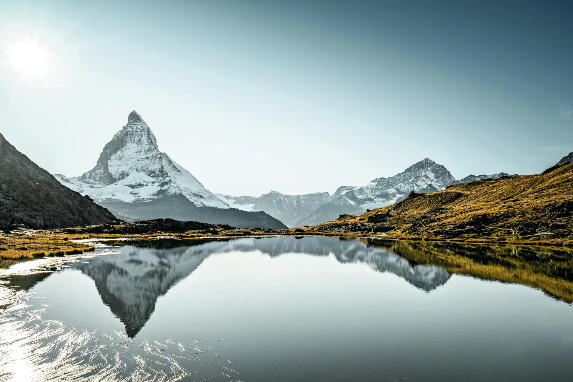 El Cervino se refleja en un lago de montaña, con un cielo azul de fondo.