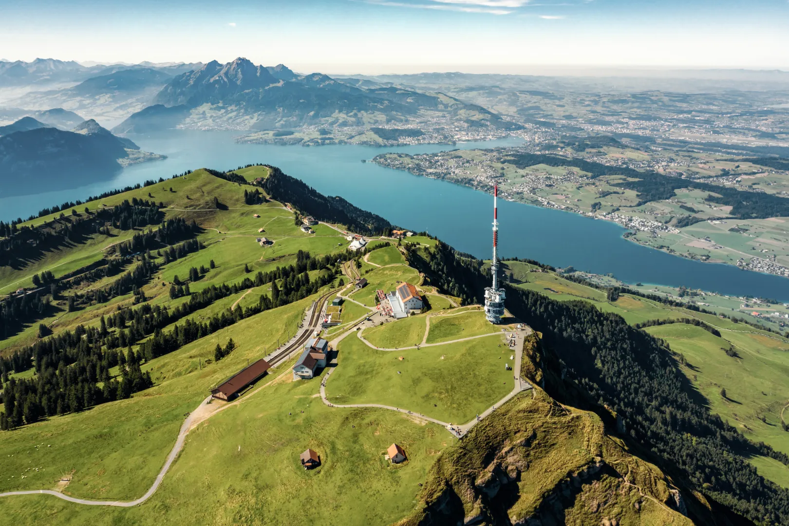 Rigi Kulm tower with surrounding green landscape, with a mountain panorama and Lake Lucerne in the background.