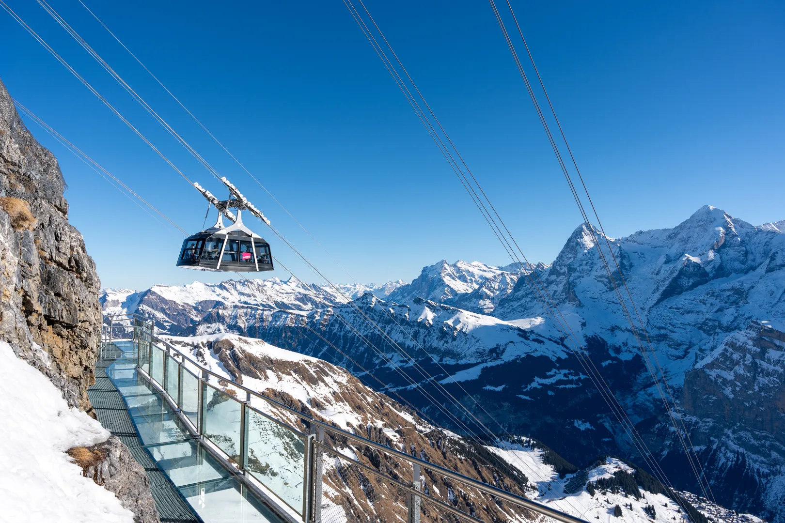 The Schilthornbahn cable car glides over the Thrill Walk, with snow-capped mountains in the background.