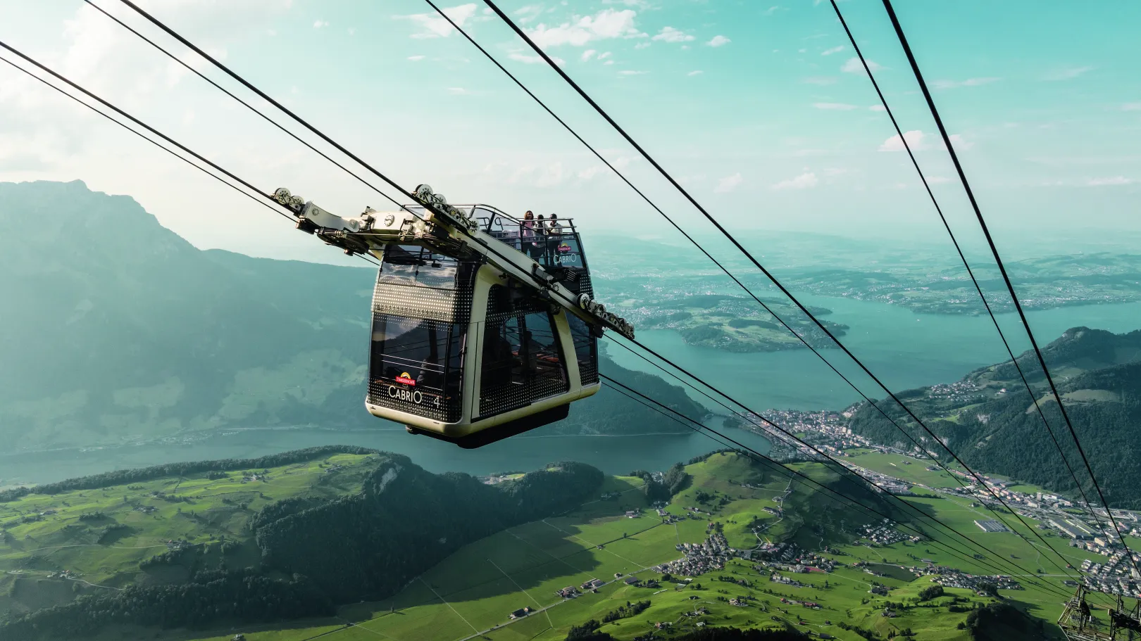 The CabriO cable car descends from the mountain station, offering views of green valleys, Lake Lucerne, and the surrounding mountain landscape.