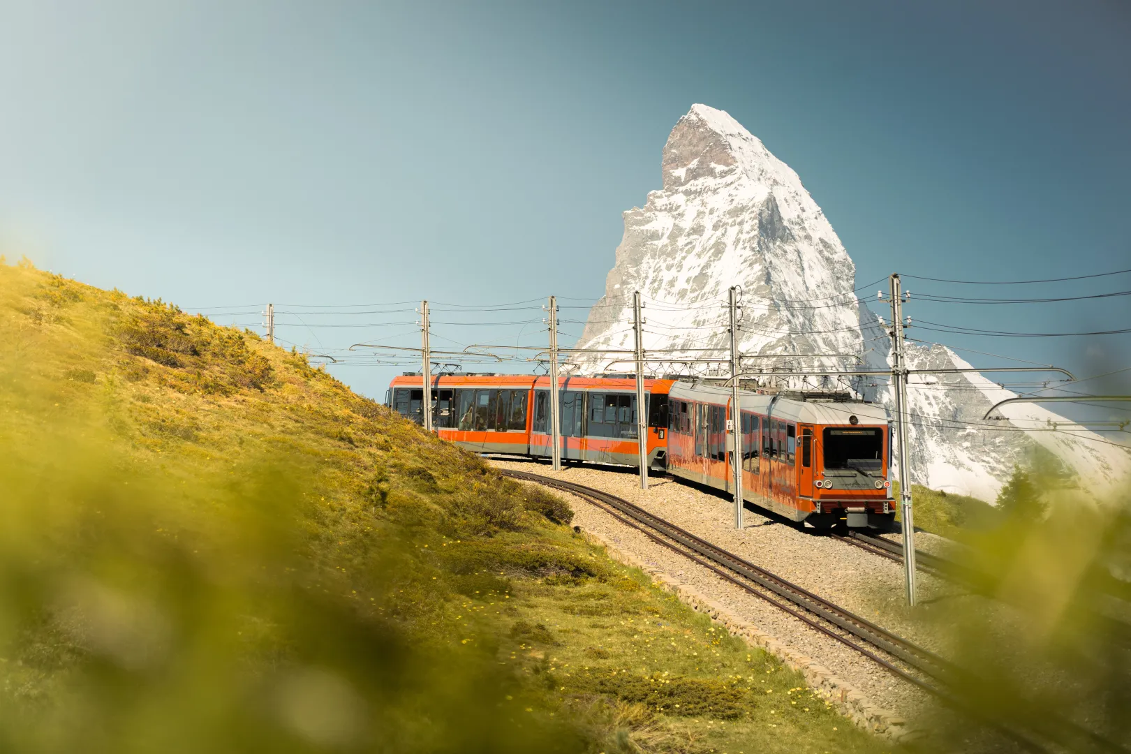 The Gornergrat Railway passes through a green alpine landscape with views of the Matterhorn.