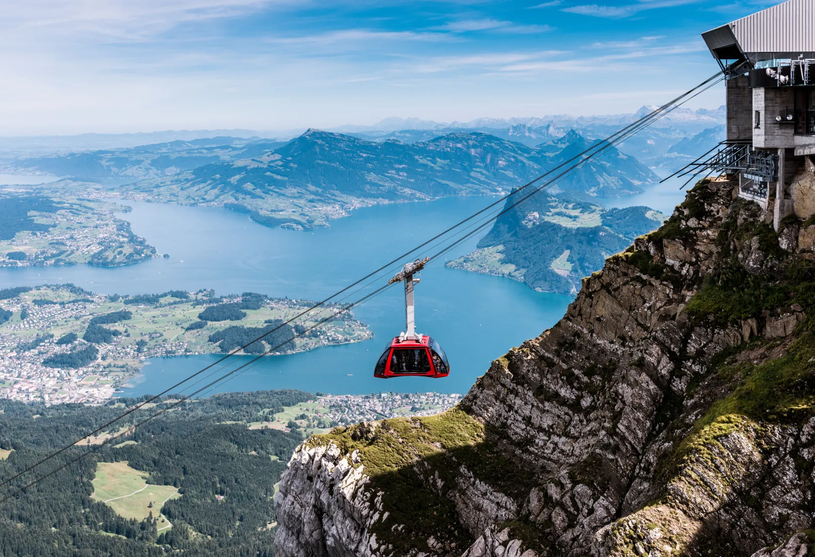 The Pilatus Dragon Ride cable car floats over steep cliffs with views of the blue Lake Lucerne.