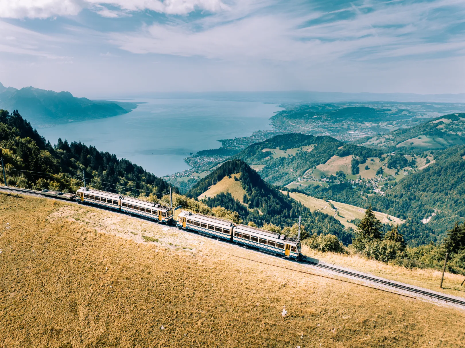 The Rochers de Naye cogwheel railway runs through green hills above Lake Geneva, with wide views of the lake and surrounding landscape.