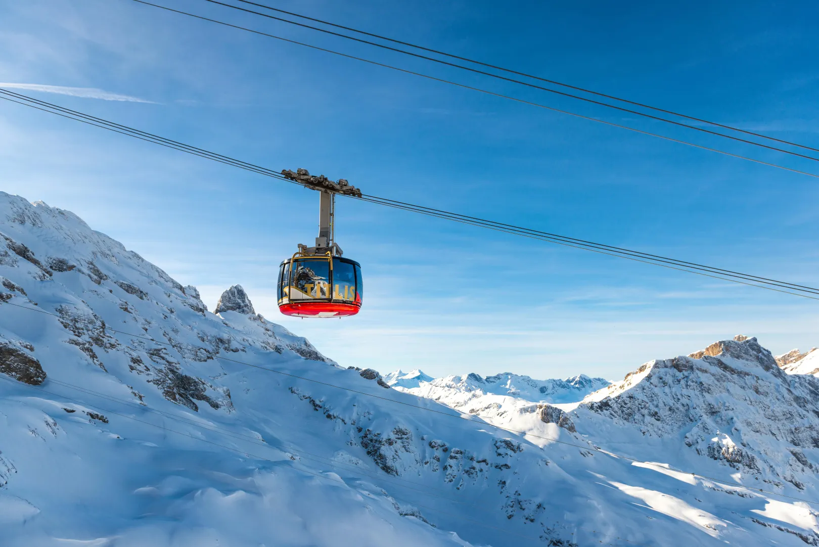 The Titlis Rotair cable car floats over a high alpine mountain landscape.