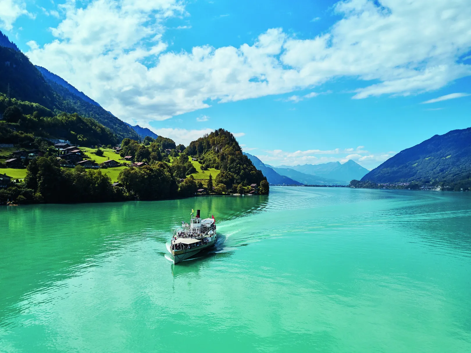 The steamship of BLS Schifffahrt sails over Lake Brienz in summer, with an alpine mountain backdrop.